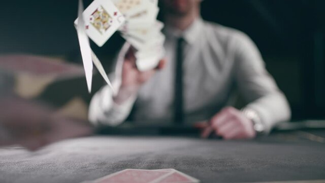 A professional croupier is working with cards. Close up of holdem dealer with playing cards on black table. Concept of casino gambling or poker and entertainment. Slow motion