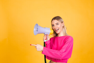 Pretty european woman in pink  blouse on yellow background happy funny screaming in megaphone cheerful excited amazed point left with finger