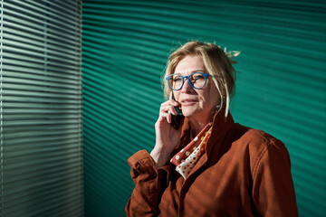 Portrait of elegant mature businesswoman talking on mobile phone against the green background