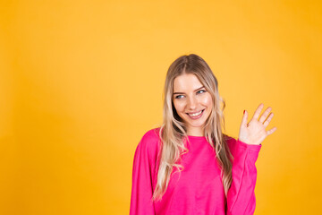 Pretty european woman in pink blouse on yellow background saying hello happy and smiling, friendly welcome gesture