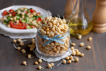 Sprouted chickpeas in glass jar. Fresh salad with tomato cucumber chickpeas and olive oil on background . Raw vegan healthy food concept. Wooden background.
