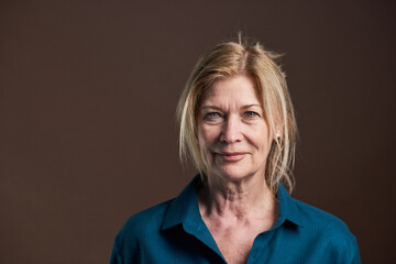 Close-up of senior woman with blond hair and in blouse looking at camera isolated on black...