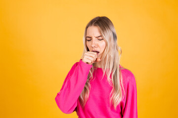 Pretty european woman in pink blouse on yellow background feeling unwell and coughing as symptom...