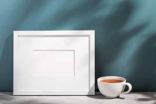 A white picture frame leans on an aegean teal painted wall.