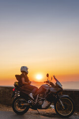 Fototapeta na wymiar Biker girl sits on a adventure motorcycle. Freedom lifestyle concept. Romantic sunset. Sea and mountains, Vertical photo. Capri island. Sorrento Italy