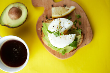 Cup of black coffee and sandwich with avocado and poached egg, seeds and microgreen. Yellow background. Copy space. Healthy breackfast