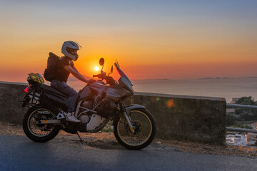 Plakat Biker girl sits on a adventure motorcycle. Freedom lifestyle concept. Romantic sunset. Sea and mountains, Copy space. Capri island. Sorrento Italy