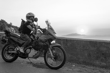 Fototapeta na wymiar Biker girl sits on a adventure motorcycle. Freedom lifestyle concept. Romantic sunset. Sea and mountains, Black and white. Capri island. Sorrento Italy