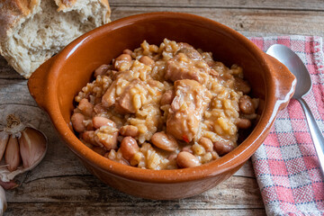 Rice with beans and meat, in a clay plate, on a rustic wooden background.