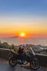 Fototapeta na wymiar Biker girl sits on a adventure motorcycle. Freedom lifestyle concept. Romantic sunset. Sea and mountains, Vertical photo. Capri island. Sorrento Italy