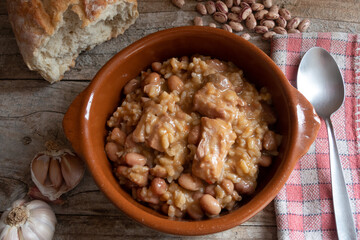 Rice with beans and meat, in a clay plate, on a rustic wooden background.