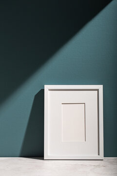 A white picture frame leans on an aegean teal painted wall.