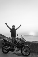 Motorcyclist man enjoy beautiful sunset arms spread out to the sides, sea and mountains. Destination. Motorcycle tour journey. vertical photo. Black and white