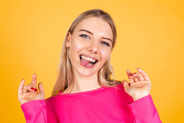 Pretty european woman in pink blouse on yellow background sticking tongue out happy with funny expression does funny grimaces