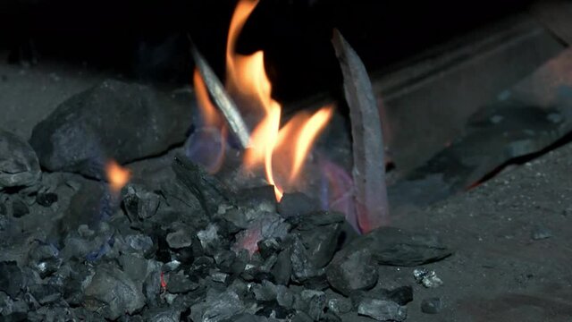 Blacksmith in a fire heats metal to forge a product. Red coals in the furnace