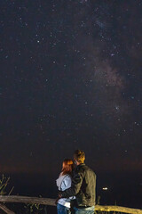 Couple traveler enjoying watched the star and milky way galaxy over the sky on top of the mountain. Night landscape with beautiful sky. Vertical photo