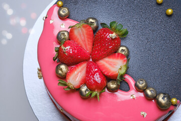 Delicious pink and dark gray birthday cake with golden berries and sweet strawberry. Selective focus.