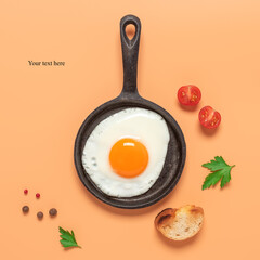 Fried egg in a frying pan on a pastel peach background with tomato, toast and spices. Creative layout. Breakfast concept. Top view, flat lay.