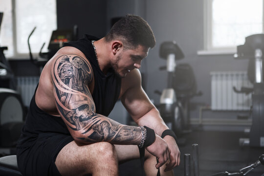 Tattooed muscular sportsman resting after exercising on seated cable rowing machine, copy space - Powered by Adobe