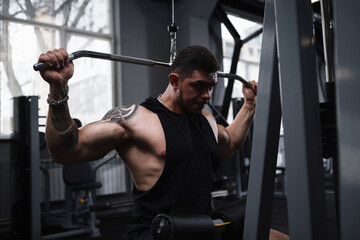 Fototapeta na wymiar Muscular strong bodybuilder exercising on vertical row lat pulldown gym machine