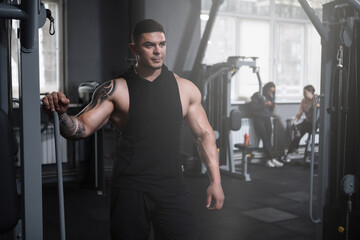 Handsome tattooed male bodybuilder resting after exercising at the gym, copy space