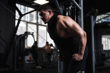 Low angle shot of a muscular sportsman doing back muscles workout in crossover gym machine