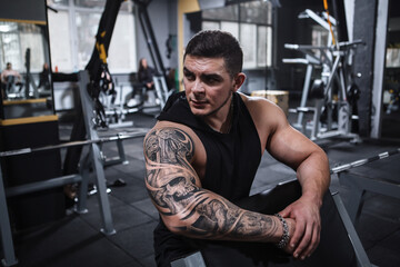 Attractive young bodybuilder looking away, resting after exercising, copy space