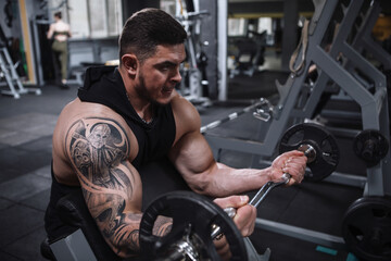 Fototapeta na wymiar Ripped tattooed sportsman doing barbell biceps curls at the gym