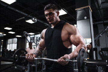 Fototapeta na wymiar Handsome muscular sportsman looking concentrated, working out with barbell at gym