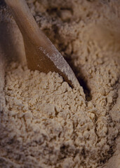 Closeup of a wooden spoon in a bowl of organic flour for baking