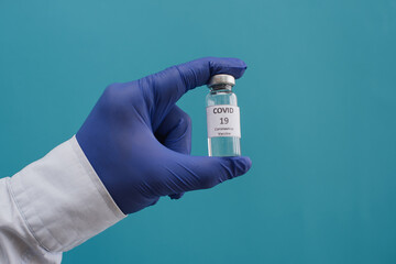 Male hands hold vial of Covid - 19 vaccine in bottle for injection on blue background. Place for text