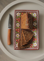 One fresh loaf of bread on a clay plate, close-up, on metal table with knife.