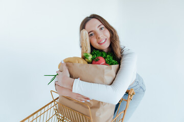 Smiling young woman in denim clothes isolated on white  wall background. Delivery service from shop or restaurant concept. Hold brown craft paper bag for takeaway mock up with food products
