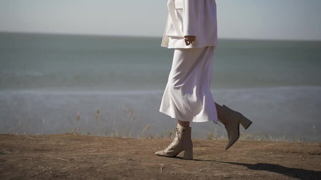 Woman in white skirt and white jacket walks along the seashore. Model gait for advertising women's clothing