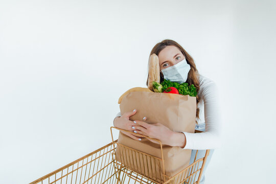 Woman With Medical Mask Holding A Shopping Bag Full Of Fresh Food. Young Woman With A Grocery Shopping Bag During Covid 19, Coronavirus Pandemic . Beautiful Young Woman With Vegetables In Grocery Bag.