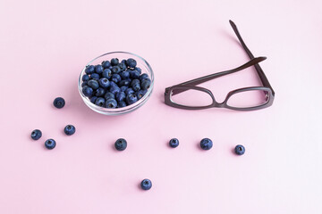 Glasses and blueberries on a pink background. Natural products to improve vision.