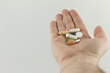 Colorful pills and tablets in a man's hand on a white background. Copy space. Medicine and healthcare concept