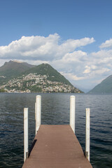 view from a small port on the lake of the city of lugano towards the populated hills, on a summer day under a blue sky