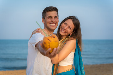 Young Couple in Love on the beach holding a Coconut drink. Smiling to the camera