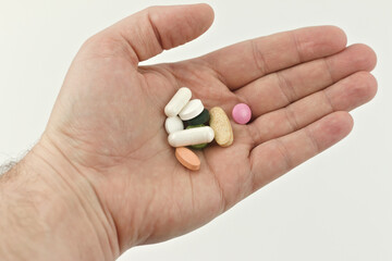 A handful of pills in a man's hand on a white background.