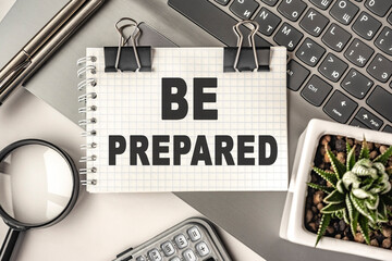 BE PREPARED text on a notepad and laptop, office tools. Business, financial concept. remote training. Coffee break, ideas, notes, goals or writing a plan, invitation concept. Top view, flat lay.