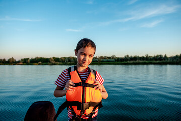 Happy boy 8 years old in a life jacket while walking on a boat. Fun holidays on the lake 