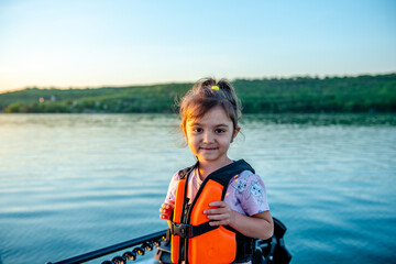 Little happy girl in a life jacket while walking on a boat 