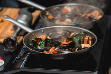 the chef prepares a seafood dish. frying pan with seafood and lemon and basil. shrimp squid and mussels fried in white.