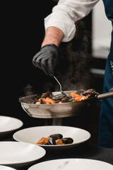 the chef prepares a seafood dish. frying pan with seafood and lemon and basil. shrimp squid and mussels fried in white.