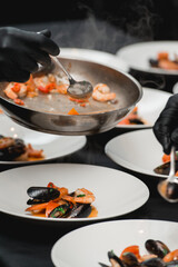 the chef prepares a seafood dish. frying pan with seafood and lemon and basil. shrimp squid and mussels fried in white.