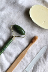 Jade face roller, wooden toothbrush, glass nail file and bar of soap. Sustainable body care products. Flat lay.