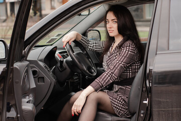 Plakat portrait of attractive brunette in grey checkered dress in a black car. girl in automobile. business woman