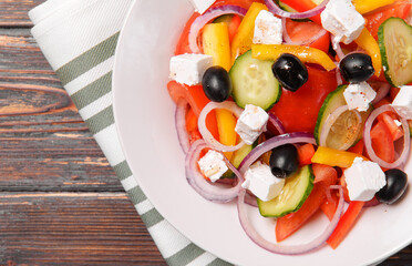 greek vegetable salad with feta tomatoes cucumber and olives in a white plate on a towel on a wooden background