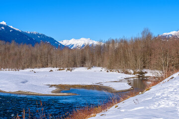 Majestic mountain river in winter over snow mountains and blue sky in Vancouver, Canada.